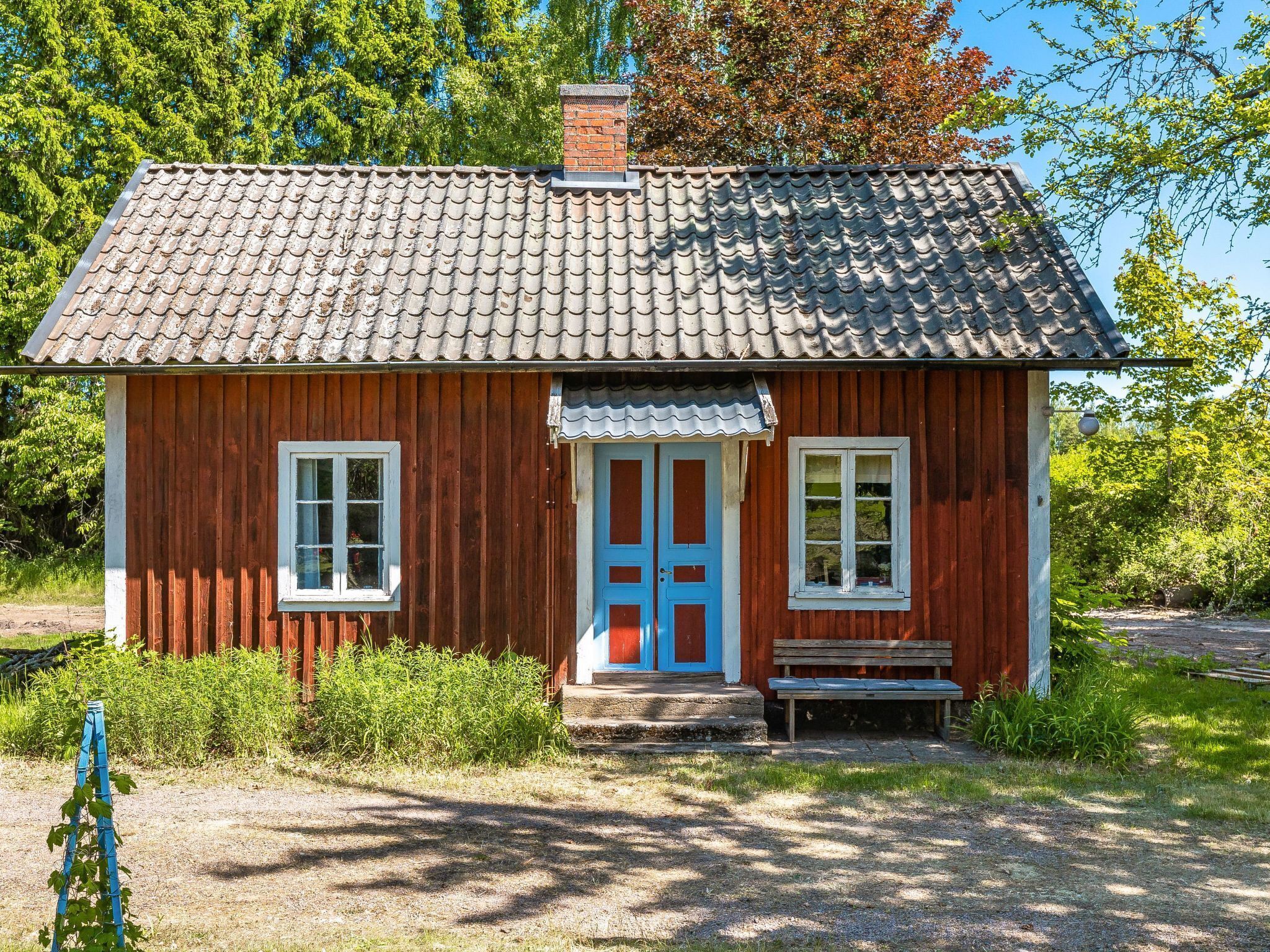 A small wooden house with a tiled roof, a blue door, and a bench outside.