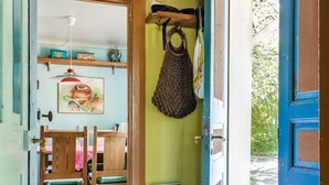 Un intérieur en bois avec un mur vert, un tapis à rayures, un sac suspendu et un banc en bois.