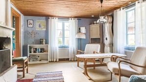 Un salon chaleureux avec un plafond en bois, une cheminée, une bibliothèque, une table à manger avec des chaises et une grande fenêtre avec des rideaux.