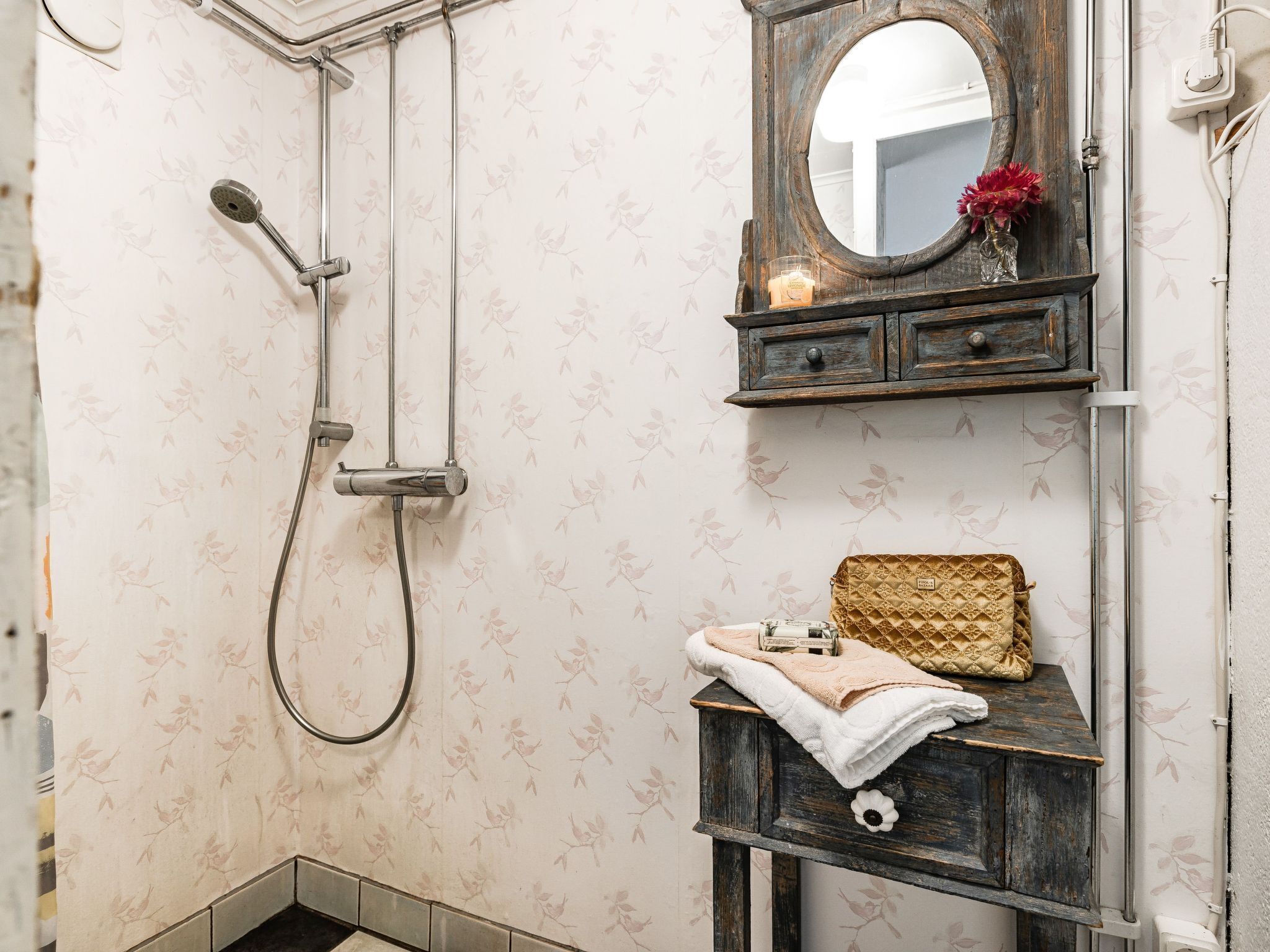 Een badkamer met een douche, een wastafel met spiegel en een decoratieve vaas.
