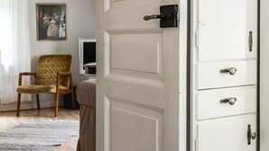 Une pièce avec une porte blanche, une chaise en bois, une armoire blanche avec des tiroirs et un tableau encadré accroché au mur.