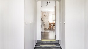 A hallway leading to a dining area with a wooden table and chairs, a clock on the wall, and a staircase with a dark floor. - Björkebo by Interhome (Ätran)