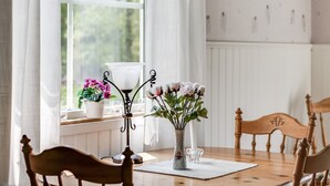 A wooden dining table with chairs, a vase with flowers, and a window with curtains. - Björkebo by Interhome (Ätran)