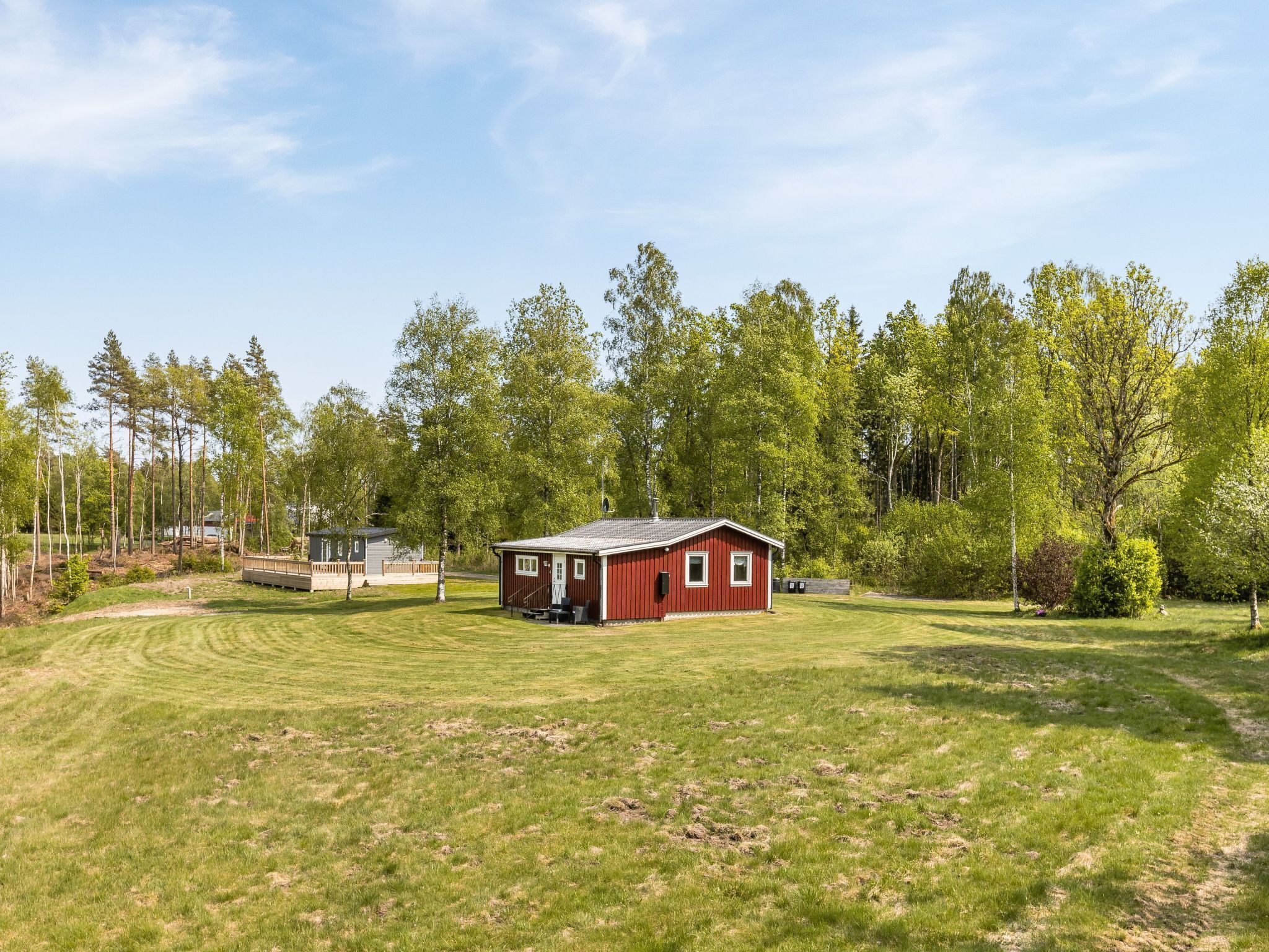 A red cabin with a porch, surrounded by a grassy field and trees.