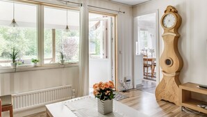 A bright room with a large window, a wooden grandfather clock, and a table with a vase of flowers. - Björkebo by Interhome (Ätran)