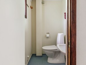 A small, narrow bathroom with a white toilet and sink, a towel rack, and a toilet paper holder on the wall.