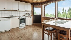 A kitchen with wooden cabinets, a stove, and a dining area with a table and chairs. - Högvallen Emma Elden by Interhome (Åre)