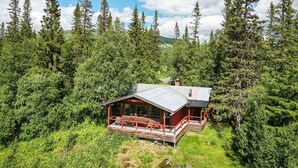 A cabin with a metal roof, wooden deck, and red railings, surrounded by dense forest and mountains. - Högvallen Emma Elden by Interhome (Åre)