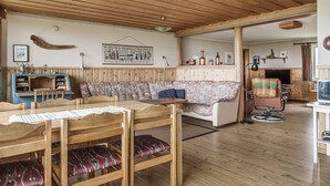 A cozy cabin interior with a wooden ceiling, a dining area with a table and chairs, a sofa with patterned cushions, and a fireplace. - Högvallen Emma Elden by Interhome (Åre)
