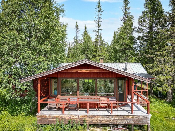 A wooden cabin with a covered deck, large windows, and a chimney.