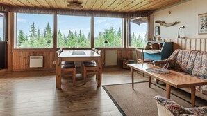 A wooden cabin interior with a dining table, chairs, a sofa, and large windows offering a forest view. - Högvallen Emma Elden by Interhome (Åre)
