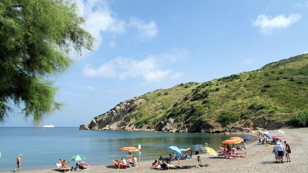 A beach with people sunbathing, umbrellas, and a boat in the water. - La Paradisa by Interhome (Nisportino)