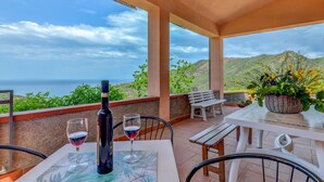 A terrace with a table set for two, a bottle of wine, and glasses, overlooking a scenic view of the sea and hills. - La Paradisa by Interhome (Nisportino)