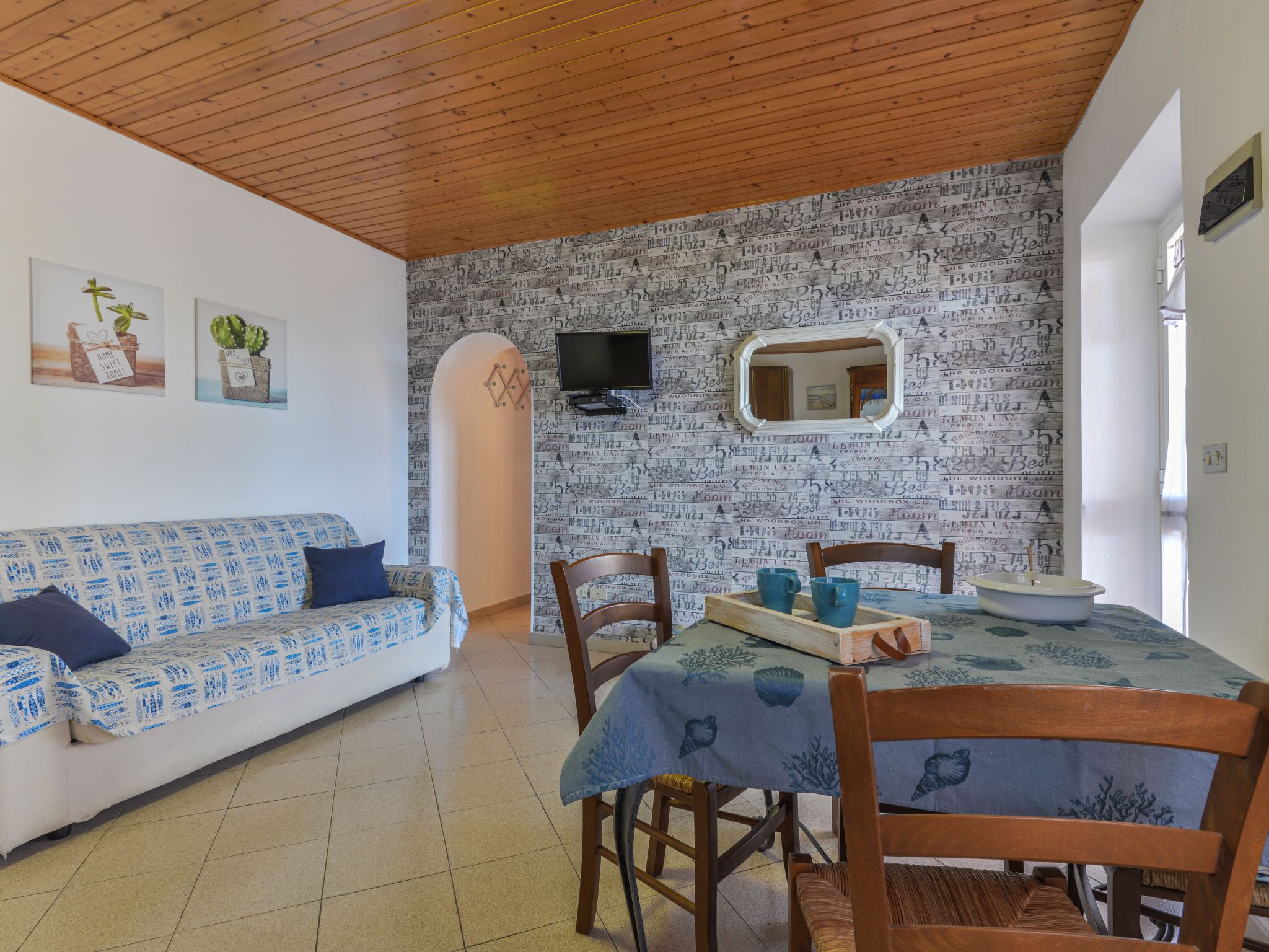 Une pièce chaleureuse avec un plafond en bois, un mur orné de motifs, un canapé, une table à manger avec des chaises et un téléviseur fixé au mur.