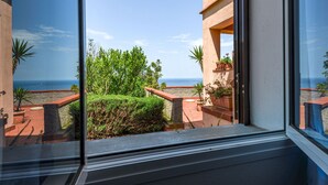Une vue depuis une fenêtre donnant sur un balcon, avec un ciel dégagé et l’océan à l’horizon.