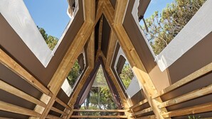 Une chambre mansardée chaleureuse avec deux lits, des poutres en bois et une vue sur les arbres.