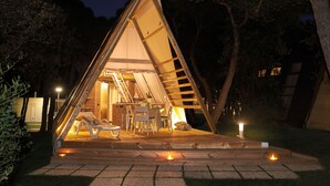 Une structure en forme de tente, dotée d’un escalier menant à un espace intérieur, le tout étant entouré d’arbres.