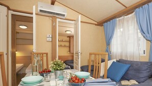 Un salon confortable avec une table à manger pour deux personnes, un canapé agrémenté de coussins et un climatiseur fixé au mur.
