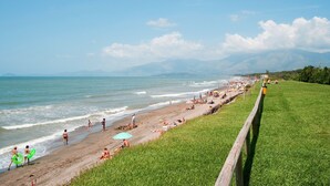 Une plage avec une zone herbeuse, une clôture en bois et l’océan en arrière-plan.