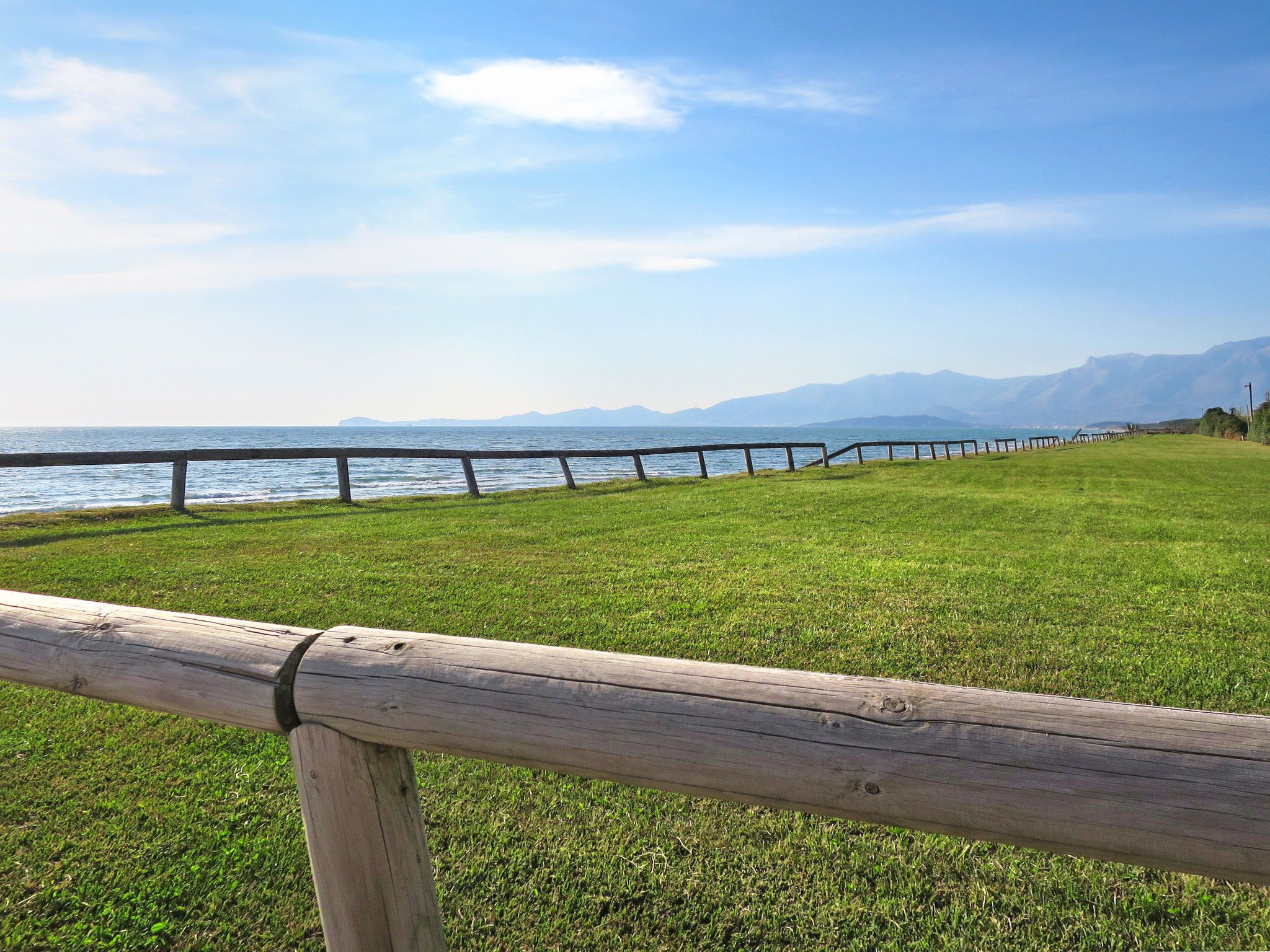 Una zona erbosa con una recinzione in legno e vista sul mare e sulle montagne.