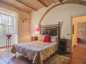 A bedroom with a bed, a nightstand, a lamp, and a window with lace curtains.