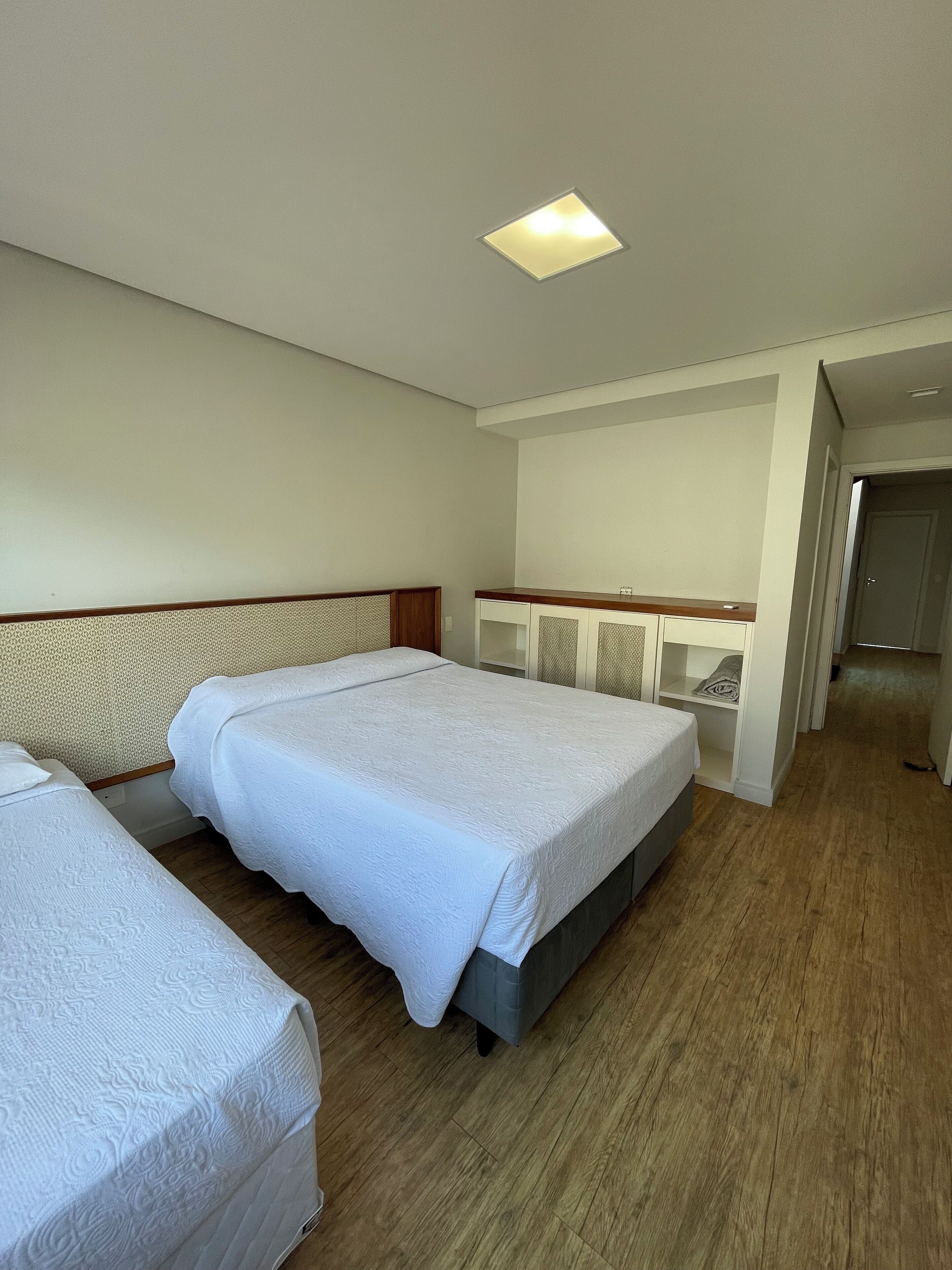 A hotel room with two beds, a wooden floor, a ceiling light, and a small desk.