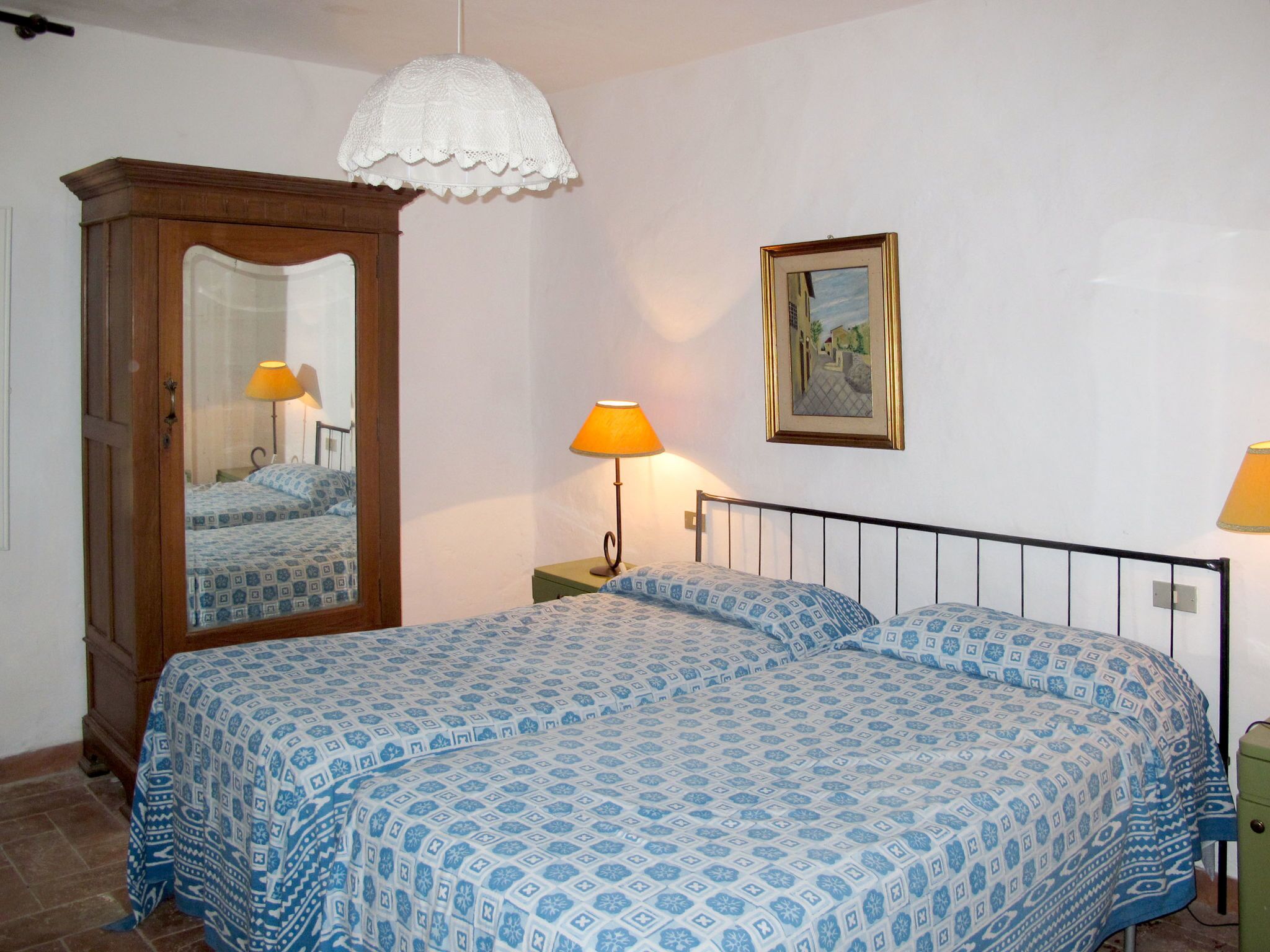 Une chambre à coucher avec un lit, une table de chevet, une lampe, un miroir et un tableau encadré accroché au mur.