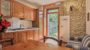 A kitchen with wooden cabinets, a stove, and a sink. There is a dining table and a sofa in the adjacent living area. - Fattoria Petraglia - Cedro by Interhome (Monteriggioni)