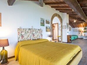 Ein Schlafzimmer mit einem Bett, einer Lampe, einem blumengemusterten Kopfteil und einer Tür zu einem anderen Raum.