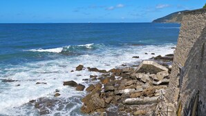 A rocky coastline with waves crashing against the shore and a clear blue sky.