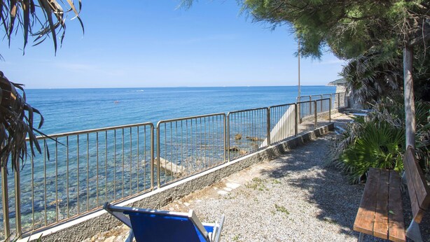 A coastal walkway with a metal railing, a wooden bench, and a clear view of the sea.