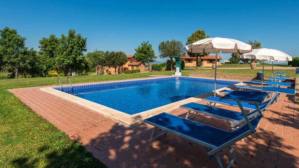 A rectangular swimming pool with a tiled edge, surrounded by a brick deck. There are lounge chairs and umbrellas on the deck. - Terrazza by Interhome (Istia d'Ombrone)