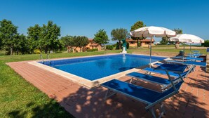 Ein rechteckiger Pool mit einer gefliesten Kante, umgeben von einer Ziegelterrasse. Auf der Terrasse stehen Liegestühle und Sonnenschirme.