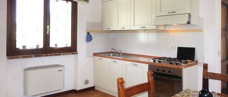 A kitchen with white cabinets, a stove, and a dining table with a bottle of wine.