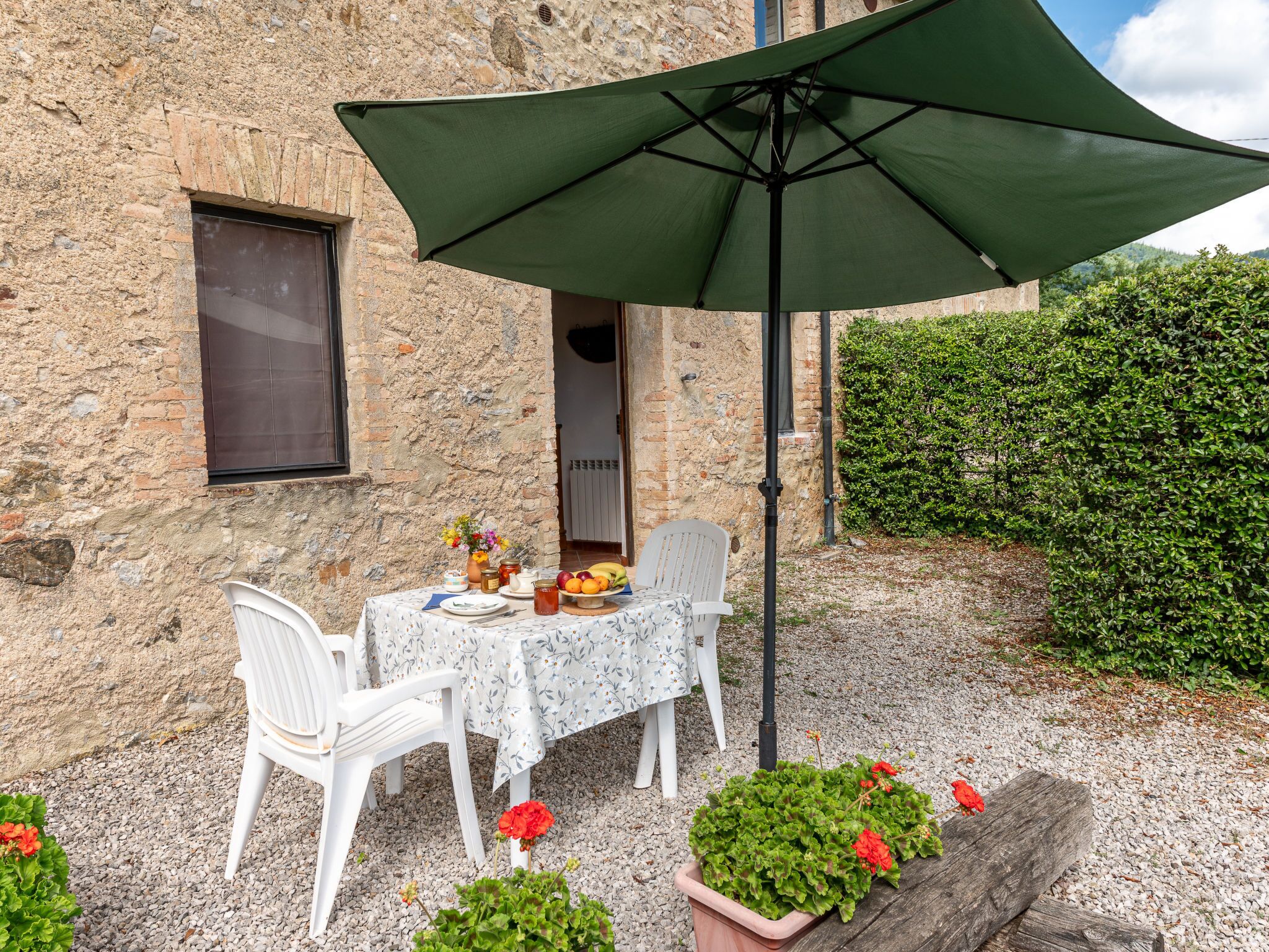 A stone building with a table set for two under a green umbrella.