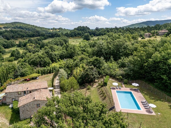 A stone villa with a swimming pool, surrounded by lush greenery and hills.