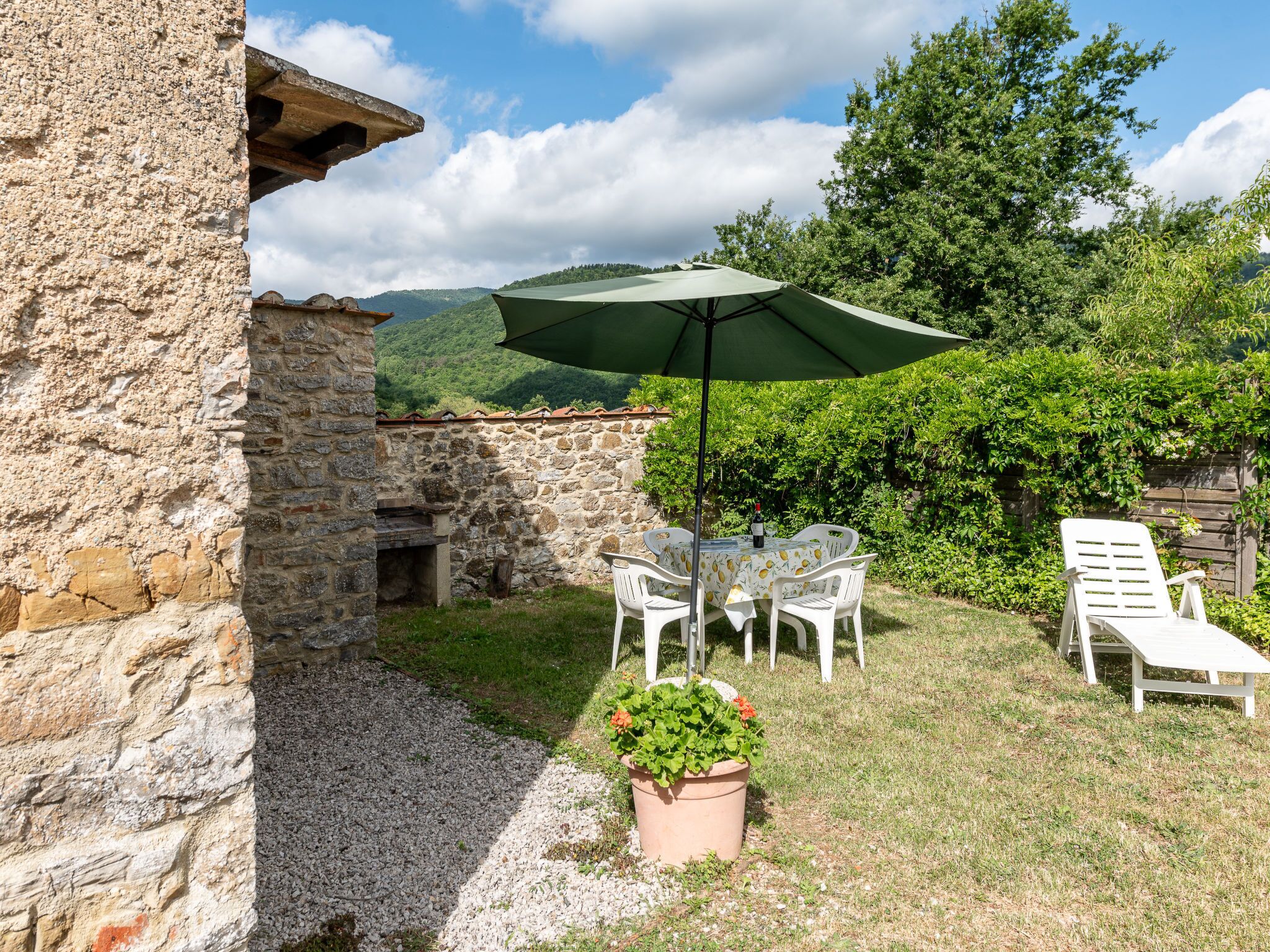 A stone building with a patio area featuring a table and chairs, a green umbrella, and a potted plant.
