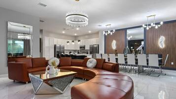 Un salon moderne avec un canapé d’angle, une table basse en verre et un coin repas doté d’un bar.