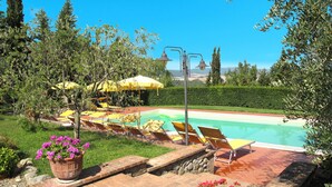 Ein Swimmingpool mit Liegestühlen und Sonnenschirmen, umgeben von viel Grün und blauem Himmel.