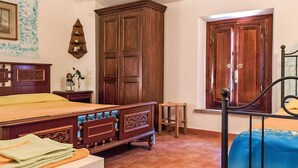 Ein Schlafzimmer mit einem hölzernen Bett, einem Kleiderschrank, einem kleinen Hocker und einem Fenster mit Holztür.