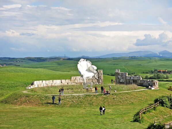 A historic site with a large white sculpture, stone ruins, and a grassy landscape with distant hills.
