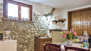 Uma cozinha rústica com parede de pedra, armários de madeira e uma mesa de jantar com cadeiras.