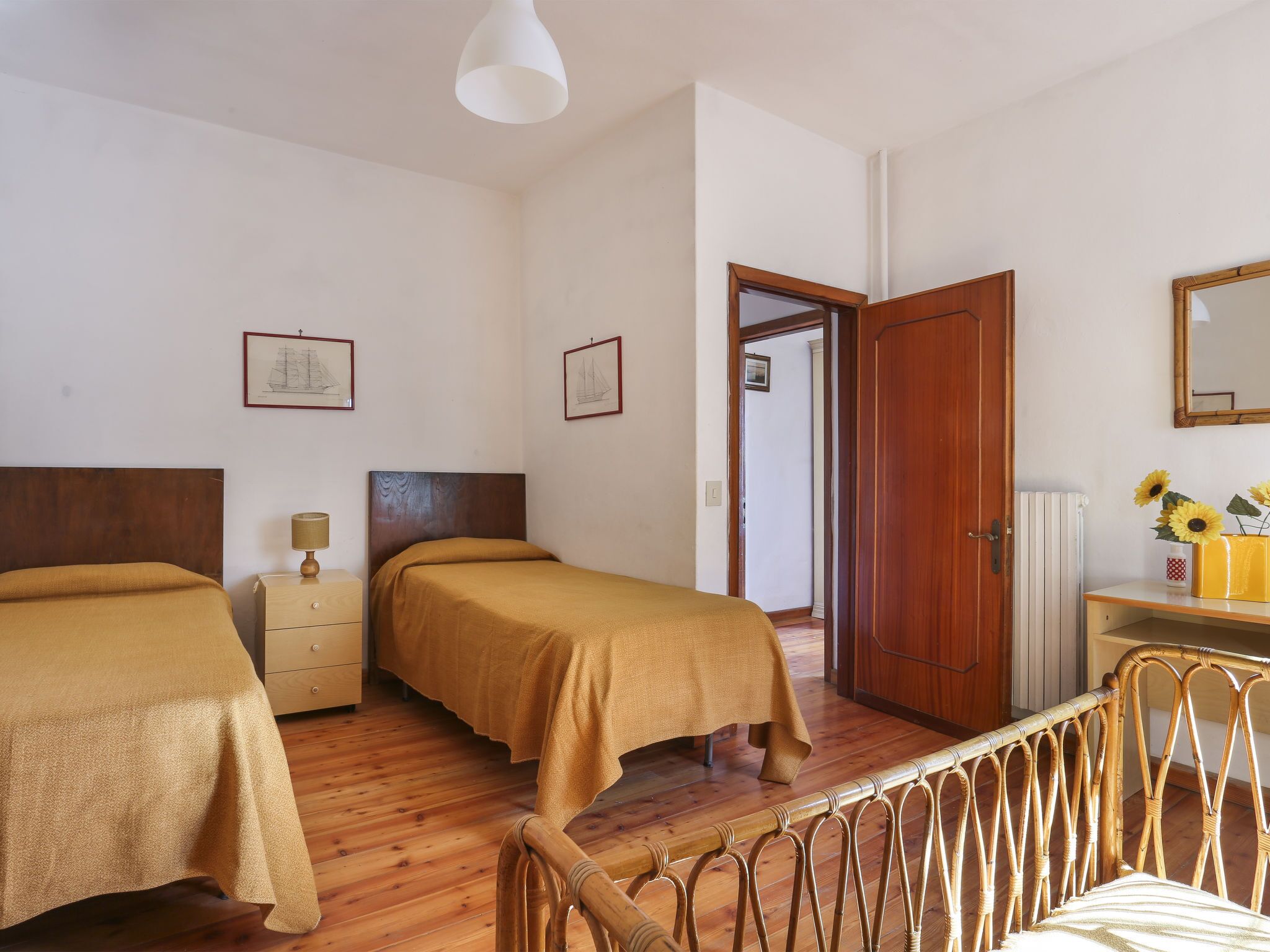A bedroom with two beds, wooden furniture, a wooden door, and a small table with a vase of sunflowers.