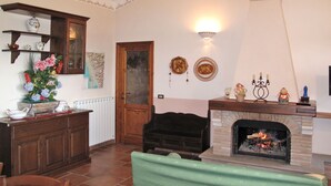 A living room with a fireplace, a wooden cabinet, a green armchair, and a dining area with a table and chairs. - Villetta degli Orti by Interhome (Gombitelli)