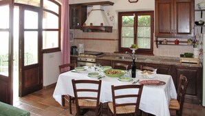 A kitchen with a dining table set for four, equipped with chairs, a coffee maker, and various kitchen appliances. - Villetta degli Orti by Interhome (Gombitelli)