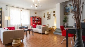 A living room with a sofa, a coffee table, and a red chair. There is a bookshelf and a dining area with a table and chairs. - La Rondine by Interhome (San Giuliano Terme)
