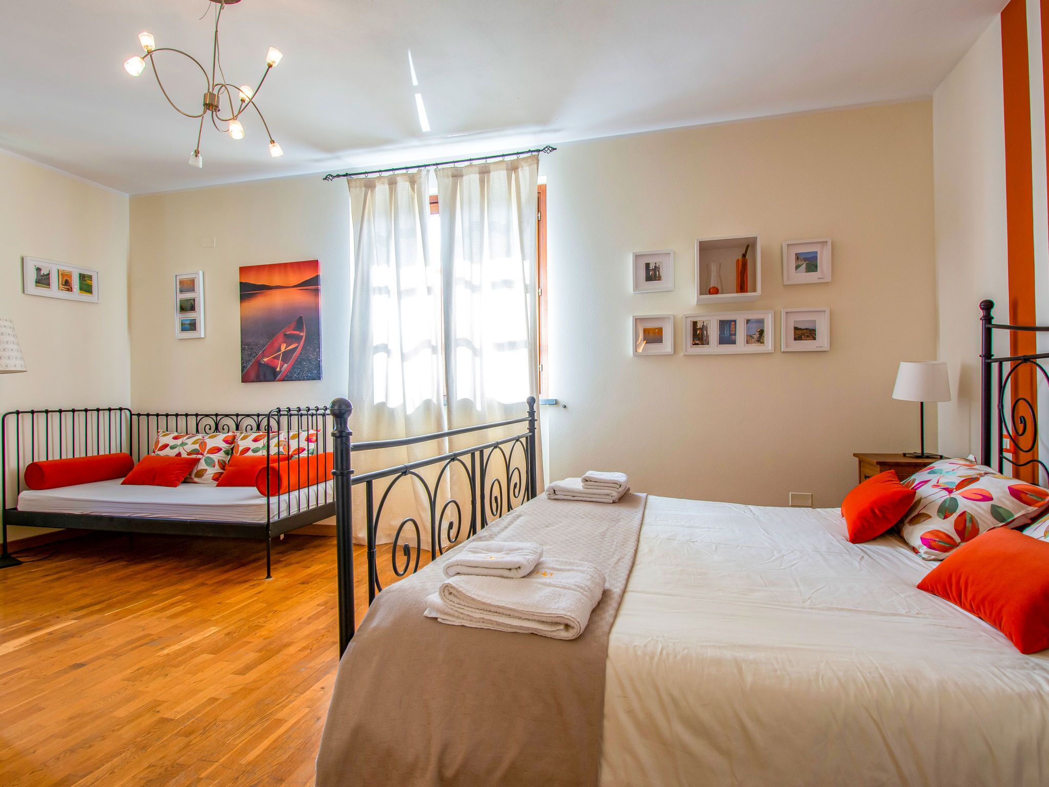 Een slaapkamer met twee bedden, een kroonluchter, een raam met gordijnen en ingelijste foto's aan de muur.