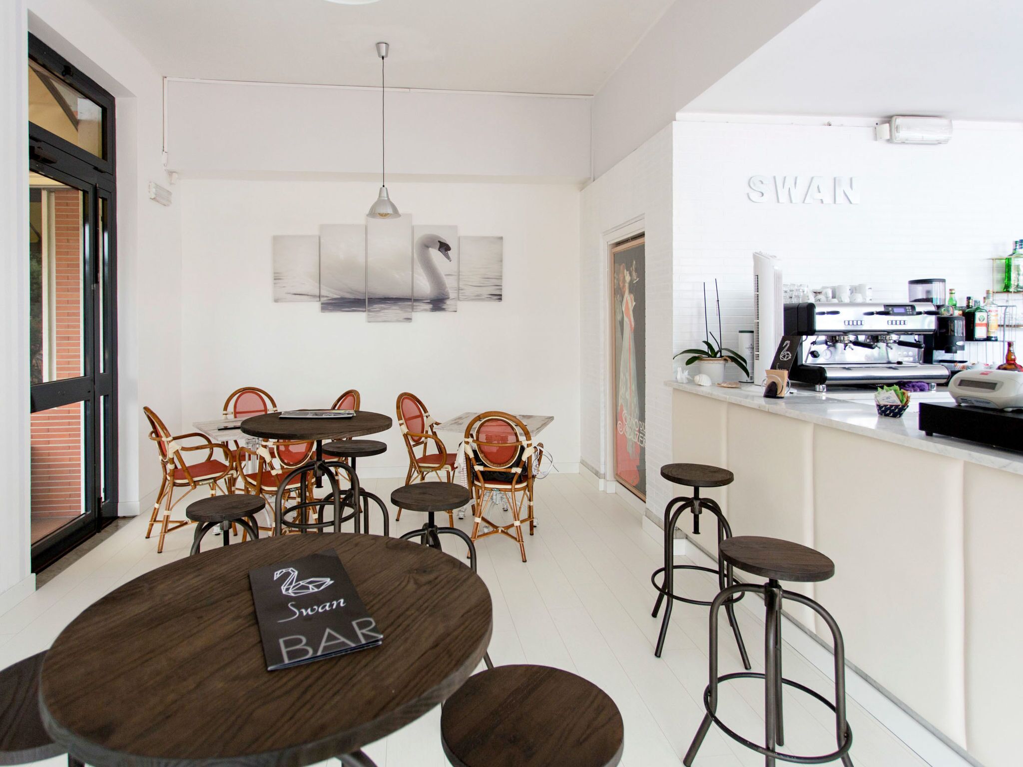 Un bar moderne avec des tables rondes et des chaises en osier, un appareil à café et une grande fenêtre.