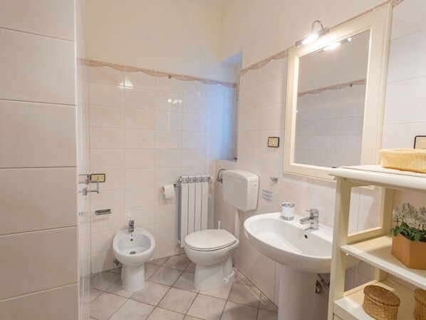 A bathroom with white tiles, a bidet, a toilet, a sink, and a mirror.