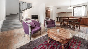 Ampla sala de estar com escada, duas poltronas roxas, uma mesa de centro de madeira e um conjunto de jantar.